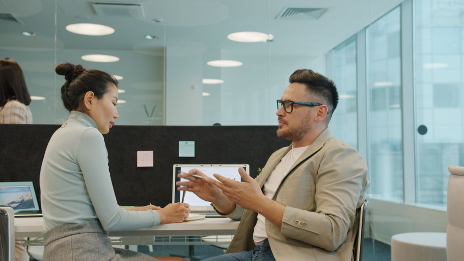 Two professionals engaged in a conversation in a modern office setting.